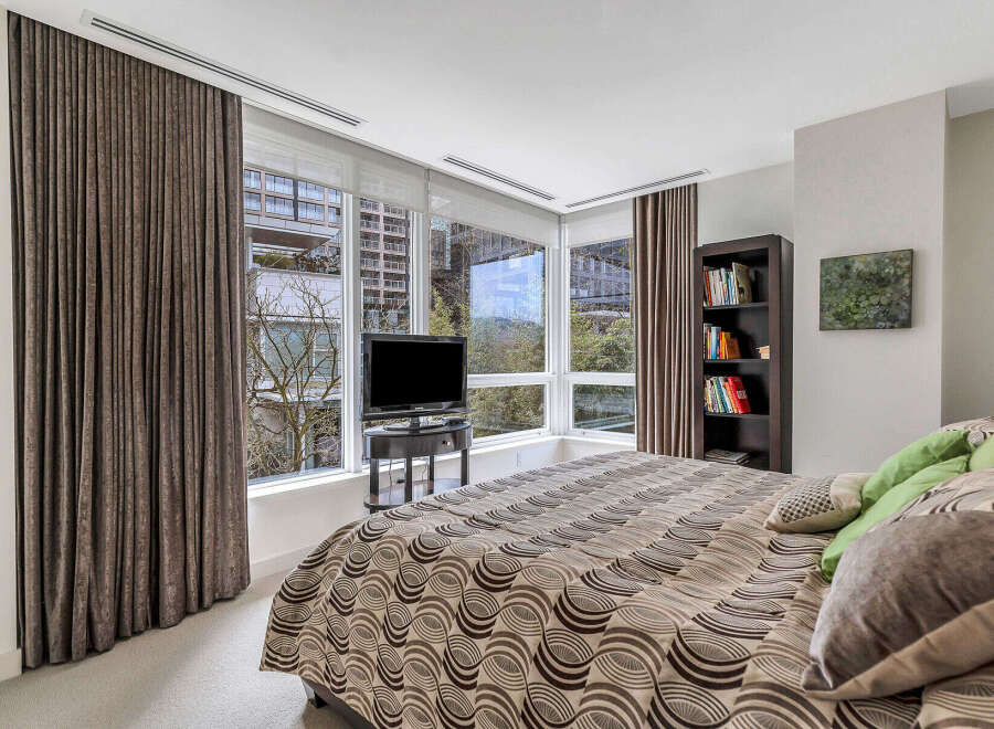 This luxurious bedroom boasts floor-to-ceiling windows offering breathtaking views, complemented by elegant brown curtains and plush carpeting.