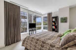 This luxurious bedroom boasts floor-to-ceiling windows offering breathtaking views, complemented by elegant brown curtains and plush carpeting.