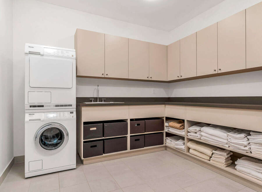 This laundry room boasts a modern design with beige cabinets, a dark countertop, and Miele washer and dryer.