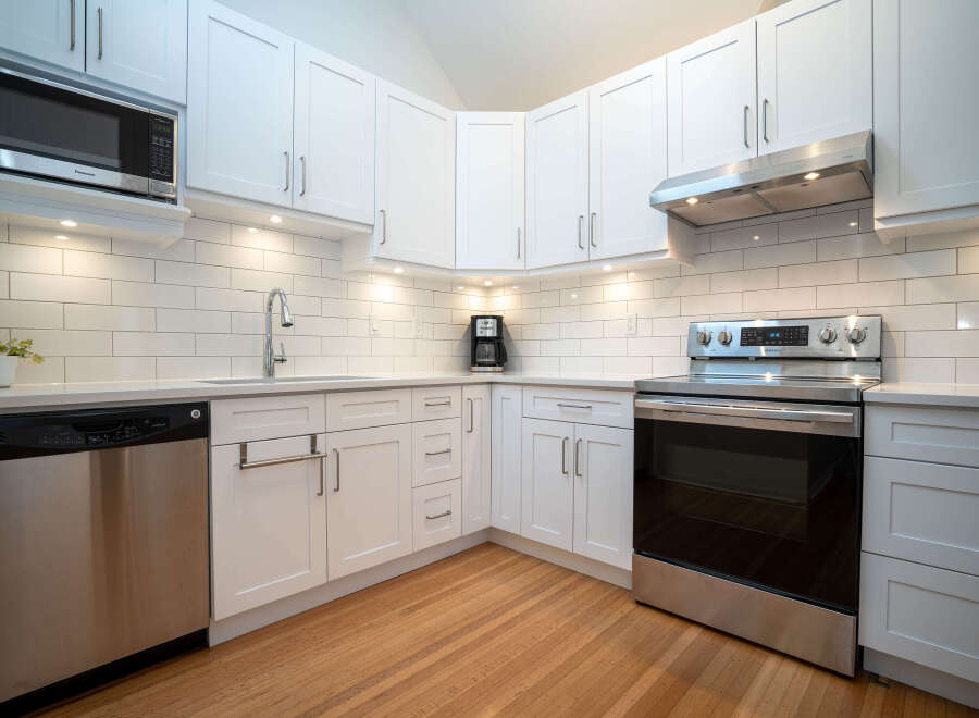 This stunning kitchen boasts modern white shaker cabinets, complemented by stainless steel appliances and sleek hardware.