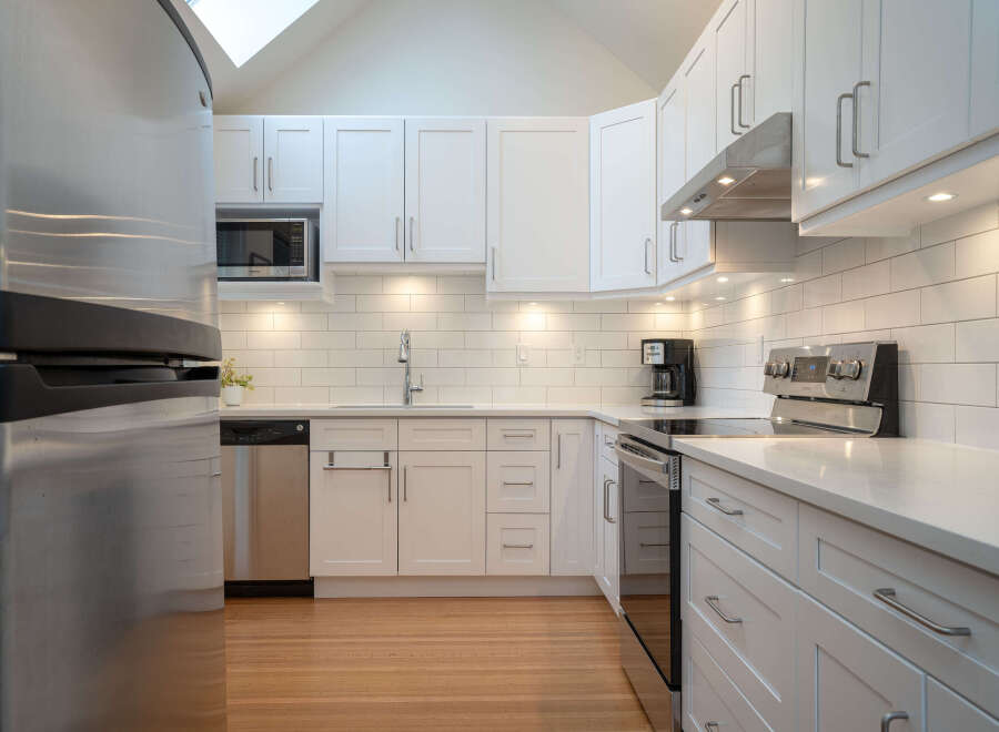 This stunning kitchen boasts modern white shaker cabinets, sleek stainless steel appliances, and a bright, airy atmosphere.