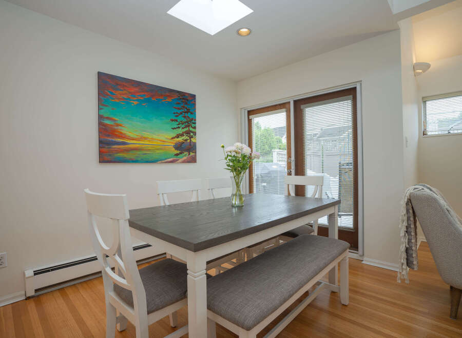 Bright dining area with hardwood floors, featuring a gray table with white chairs and bench seating.