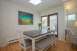 Bright dining area with hardwood floors, featuring a gray table with white chairs and bench seating.
