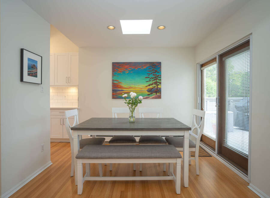 Bright dining area with hardwood floors, white table and bench seating, and a large window offering natural light.