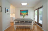 Bright dining area with hardwood floors, white table and bench seating, and a large window offering natural light.