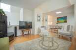 Bright and airy living room with hardwood floors, featuring a cozy seating area with two armchairs and a glass coffee table.