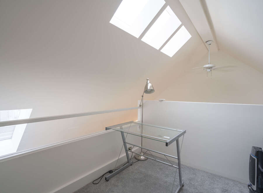 This bright loft-style room features a glass desk perfect for a home office, complemented by a stylish desk lamp.