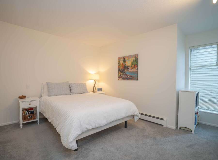 This bright and airy bedroom features a comfortable queen-sized bed with crisp white linens, complemented by a neutral color palette.