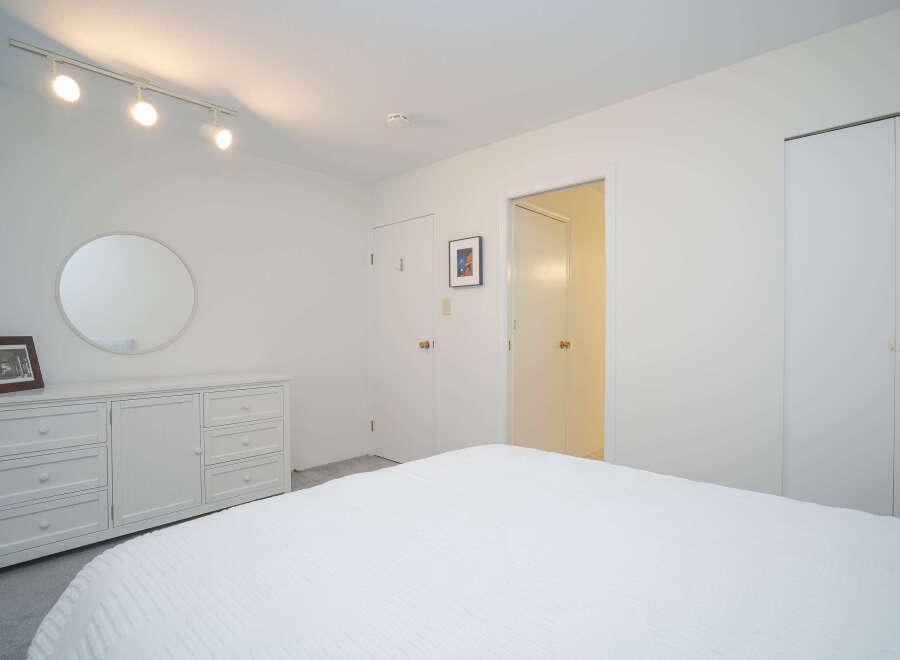 This bright and airy bedroom boasts a clean, minimalist aesthetic with white walls, a white dresser, and a crisp white duvet.