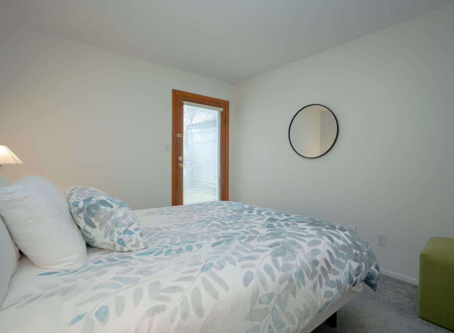 This bright bedroom features a comfortable bed with a leaf patterned duvet, plush pillows, and a bedside lamp.