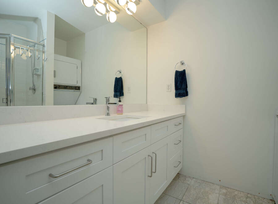 This bright bathroom boasts a modern vanity with white shaker cabinets and sleek silver hardware, complemented by a quartz countertop and an integrated sink.