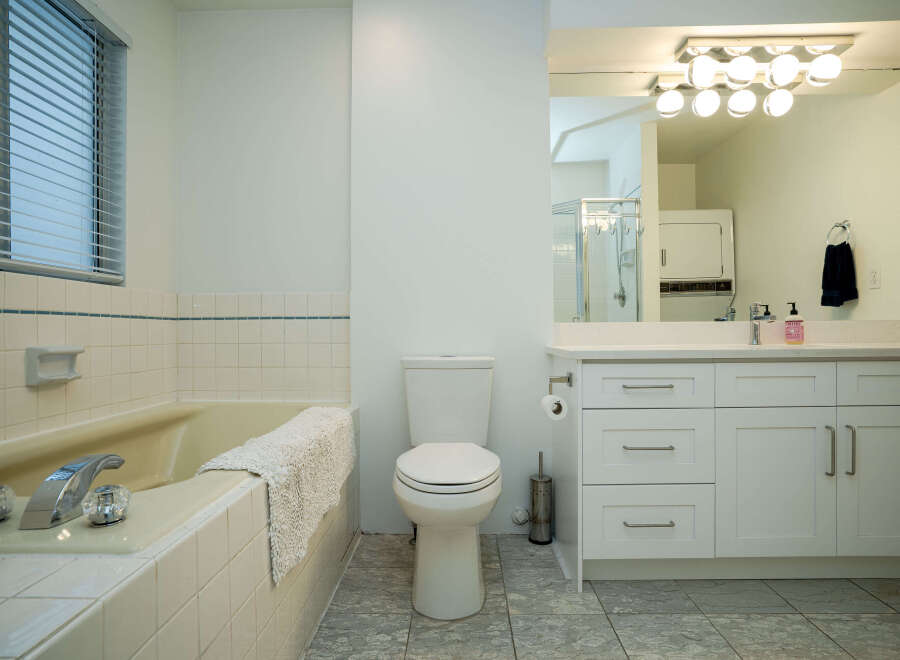 This bright bathroom boasts a classic white vanity with ample storage, complemented by a clean white toilet and a relaxing bathtub.