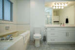 This bright bathroom boasts a classic white vanity with ample storage, complemented by a clean white toilet and a relaxing bathtub.