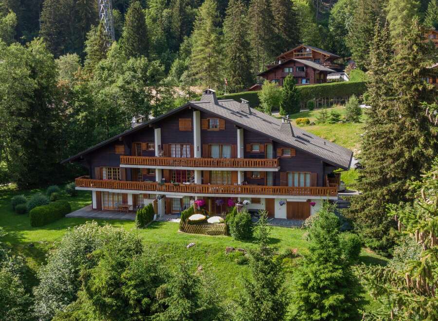 Nestled in a lush, green landscape, this stunning property boasts a classic chalet design with multiple levels and balconies.