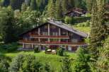 Nestled in a lush, green landscape, this stunning property boasts a classic chalet design with multiple levels and balconies.