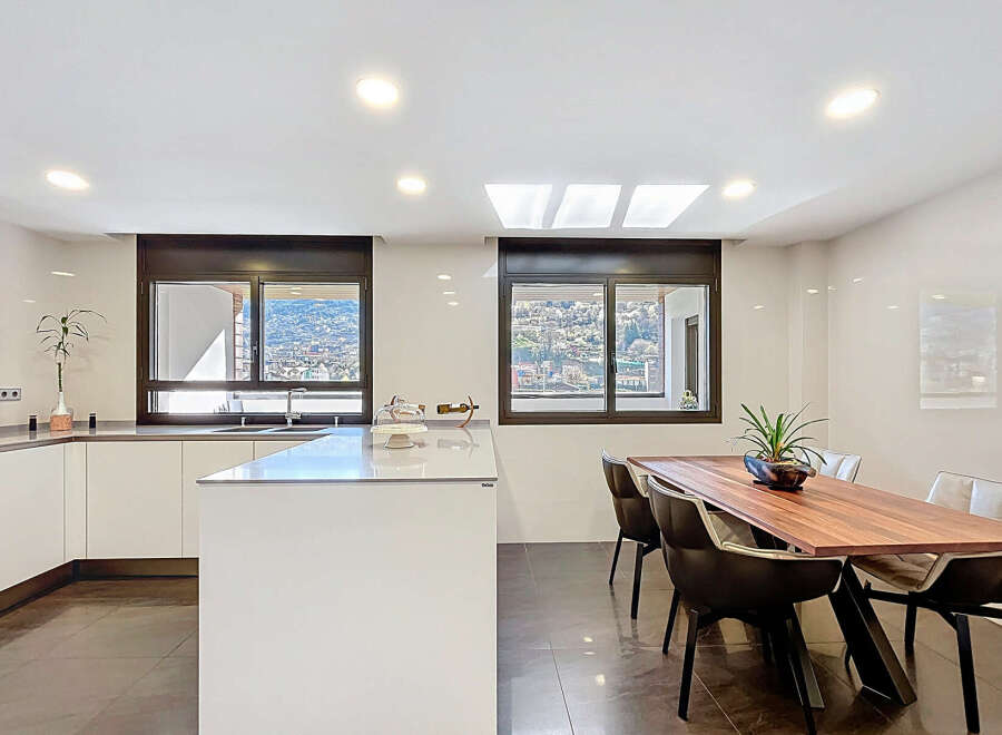 Modern kitchen with sleek white cabinetry and stunning mountain views from large windows.