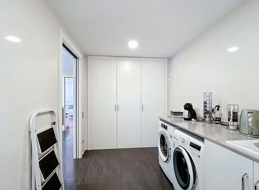 This stunning property boasts a modern laundry room with sleek white cabinetry and high-end appliances.