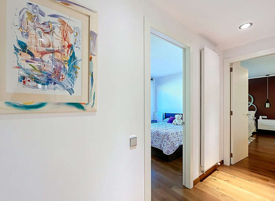 This stunning property boasts a hallway adorned with modern art, leading to a bright and airy bedroom with a comfortable bed and plush pillows.