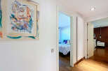 This stunning property boasts a hallway adorned with modern art, leading to a bright and airy bedroom with a comfortable bed and plush pillows.