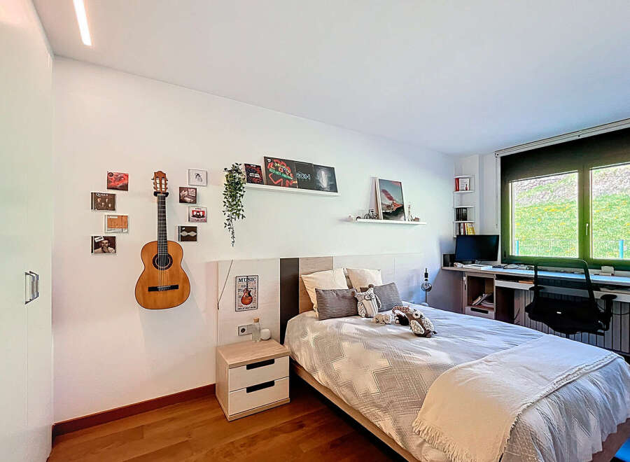 Cozy bedroom with built-in desk and window overlooking a lush green landscape.
