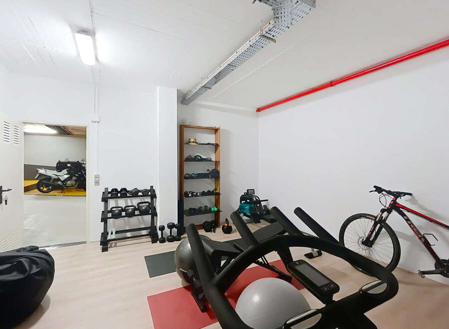 This home gym boasts an array of equipment, including weights, kettlebells, a rowing machine, and an exercise bike, perfect for a comprehensive workout.