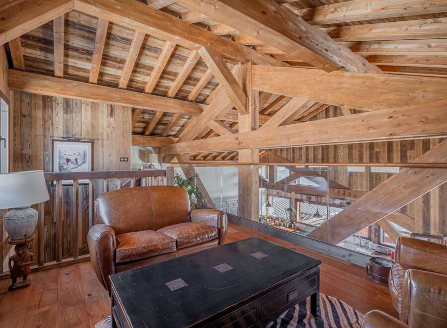 This stunning chalet boasts a breathtaking open-plan living area with exposed wooden beams and a cozy leather sofa.