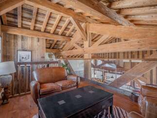 This stunning chalet boasts a breathtaking open-plan living area with exposed wooden beams and a cozy leather sofa.