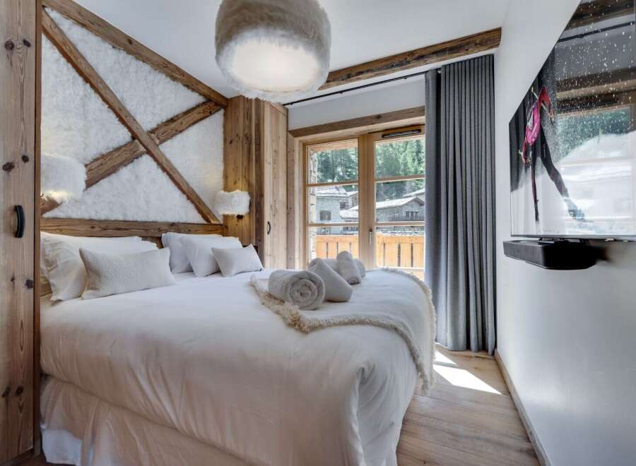 Cozy up in this luxurious chalet bedroom, featuring a plush king-size bed, a stunning wooden wall accent, and a large flat-screen TV for ultimate relaxation.