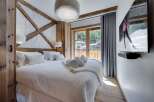 Cozy up in this luxurious chalet bedroom, featuring a plush king-size bed, a stunning wooden wall accent, and a large flat-screen TV for ultimate relaxation.