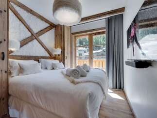 Cozy up in this luxurious chalet bedroom, featuring a plush king-size bed, a stunning wooden wall accent, and a large flat-screen TV for ultimate relaxation.