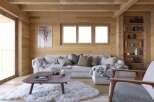 Cozy mountain cabin living room with wood-paneled walls, large windows, and a comfortable sectional sofa.