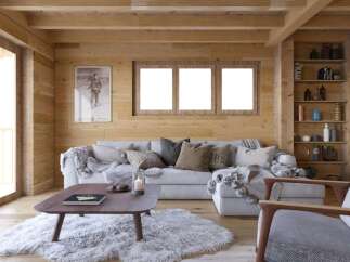 Cozy mountain cabin living room with wood-paneled walls, large windows, and a comfortable sectional sofa.