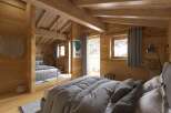 Cozy chalet bedroom with wooden walls and beams, featuring a comfortable bed with gray linens and a mirrored closet.