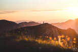 Silhouetted figures stand atop a majestic mountain peak, bathed in the golden light of a breathtaking sunset.