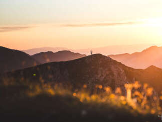Silhouetted figures stand atop a majestic mountain peak, bathed in the golden light of a breathtaking sunset.