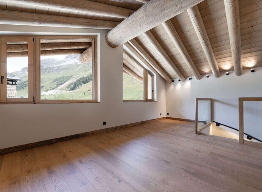 Experience breathtaking mountain views from this stunning attic room, featuring a rustic wooden beamed ceiling and expansive windows.
