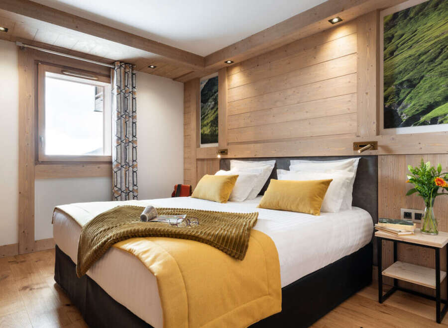 This stunning bedroom boasts a king-size bed with plush bedding, a cozy mustard yellow throw, and a wooden headboard.
