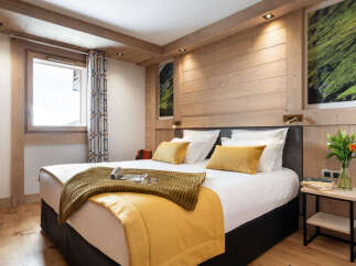 This stunning bedroom boasts a king-size bed with plush bedding, a cozy mustard yellow throw, and a wooden headboard.
