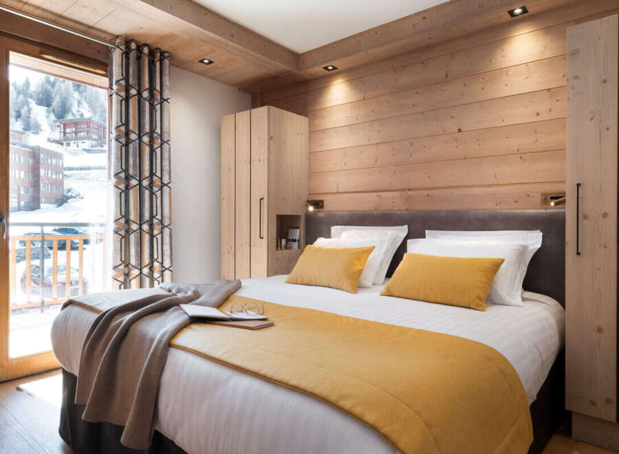 This stunning bedroom boasts a cozy wooden interior, complete with a plush bed dressed in luxurious linens and a warm-toned throw.