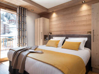 This stunning bedroom boasts a cozy wooden interior, complete with a plush bed dressed in luxurious linens and a warm-toned throw.