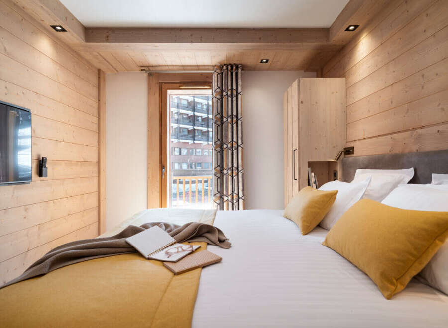 This stunning bedroom boasts a cozy wooden interior, complete with a comfortable king-size bed dressed in luxurious linens and plush mustard-yellow pillows.