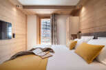 This stunning bedroom boasts a cozy wooden interior, complete with a comfortable king-size bed dressed in luxurious linens and plush mustard-yellow pillows.