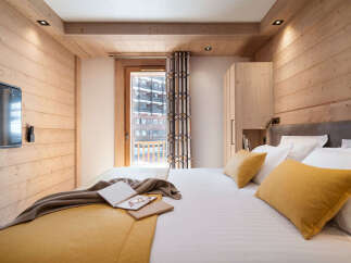This stunning bedroom boasts a cozy wooden interior, complete with a comfortable king-size bed dressed in luxurious linens and plush mustard-yellow pillows.