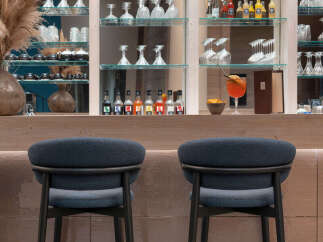 Modern bar with sleek, dark-colored bar stools and a back wall of glass shelving displaying an array of wine and liquor bottles.