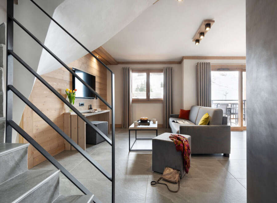 This stunning apartment boasts a spacious living area with a comfortable grey sofa, perfect for relaxing after a day on the slopes.