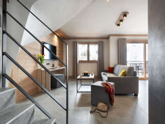 This stunning apartment boasts a spacious living area with a comfortable grey sofa, perfect for relaxing after a day on the slopes.