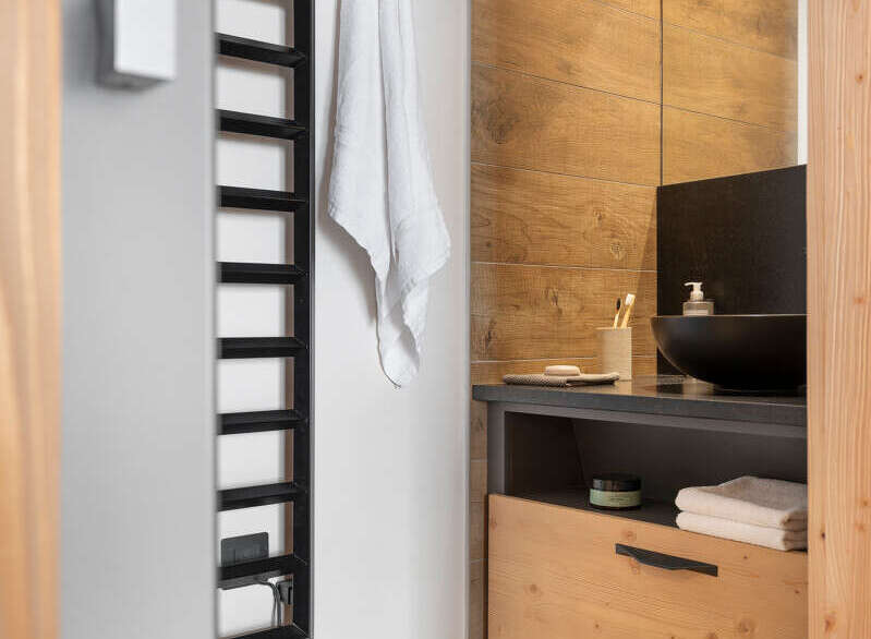 This modern bathroom boasts a sleek black heated towel rack, a stylish wooden vanity with ample storage, and a contemporary sink.