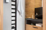 This modern bathroom boasts a sleek black heated towel rack, a stylish wooden vanity with ample storage, and a contemporary sink.