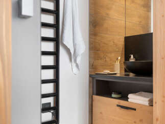 This modern bathroom boasts a sleek black heated towel rack, a stylish wooden vanity with ample storage, and a contemporary sink.