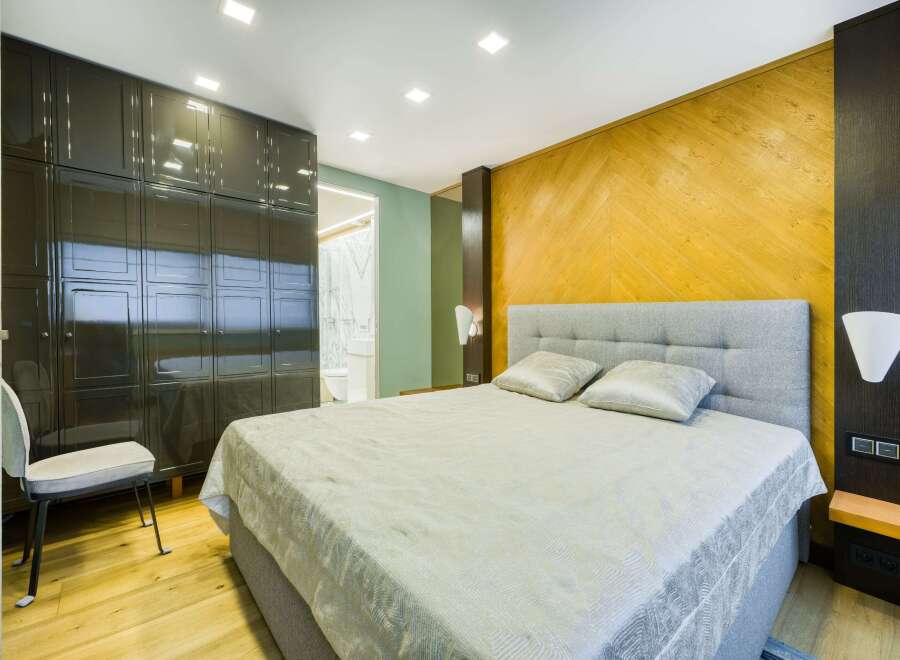 This luxurious bedroom boasts a spacious design with built-in dark wood closets and a light gray upholstered bed.